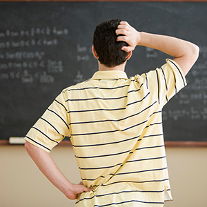 Student standing in front of a chalkboard with writing on it