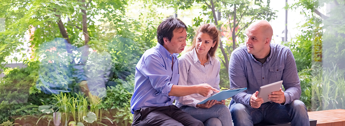 Three individuals sitting on a bench with green trees behind them