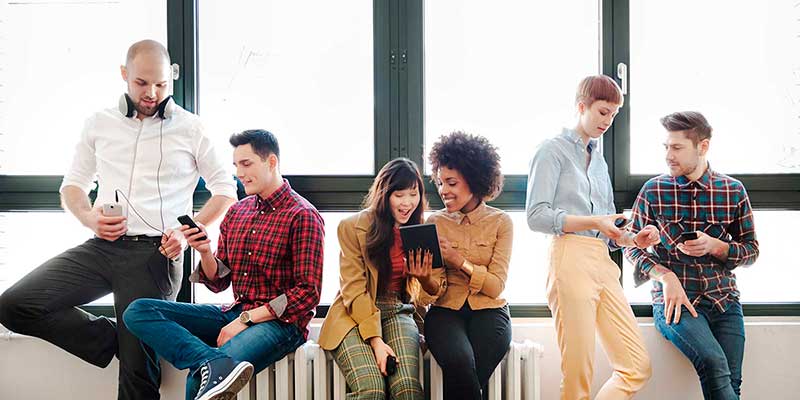 Young professionals in front of a row of windows, looking at mobile devices together