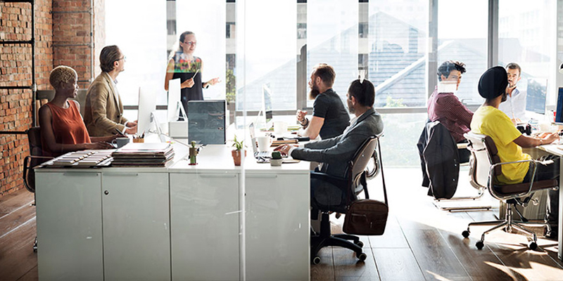 Co-workers meeting in an open, modern office with a wall of windows