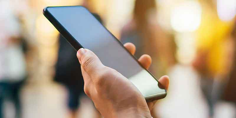 A hand holding a smartphone, with a blurred crowd in the background