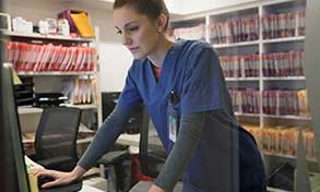 Nurse in an office with lots of files on shelves, using a computer