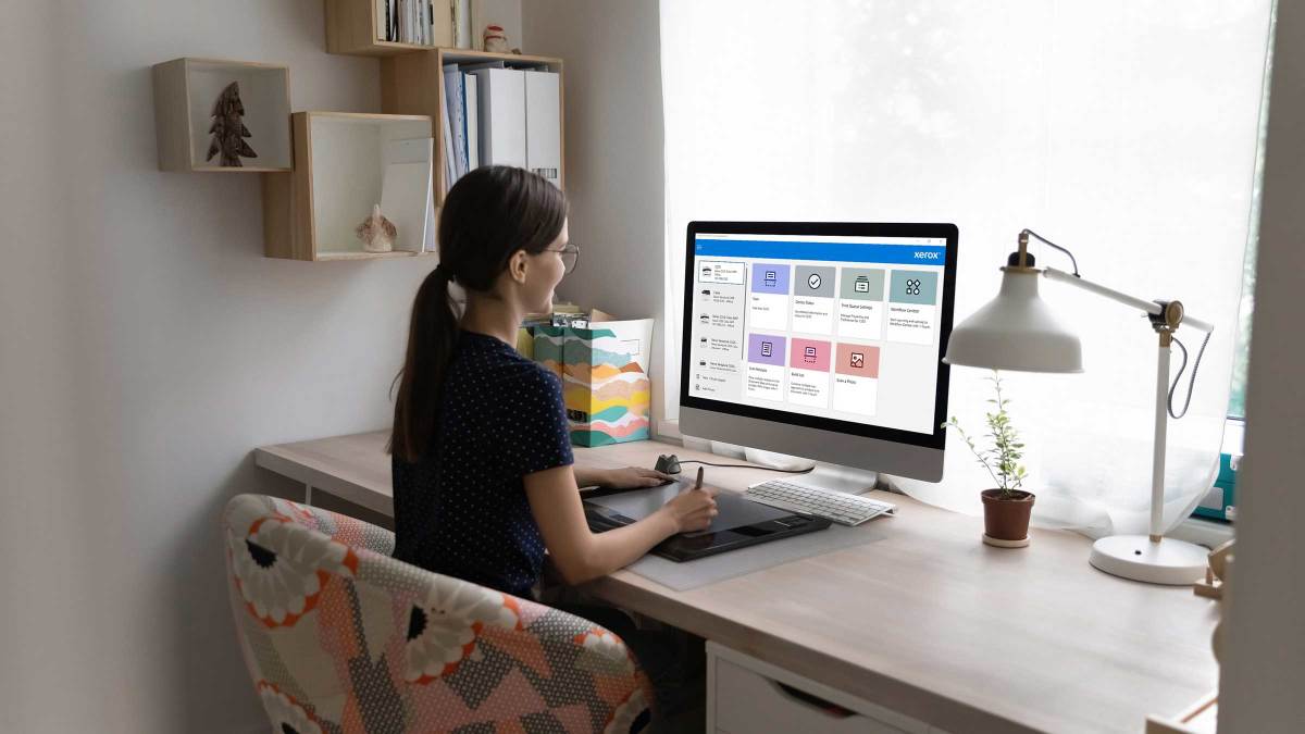 Young professional sitting at a desk by a window, working on a monitor with Xerox Print and Scan Experience App