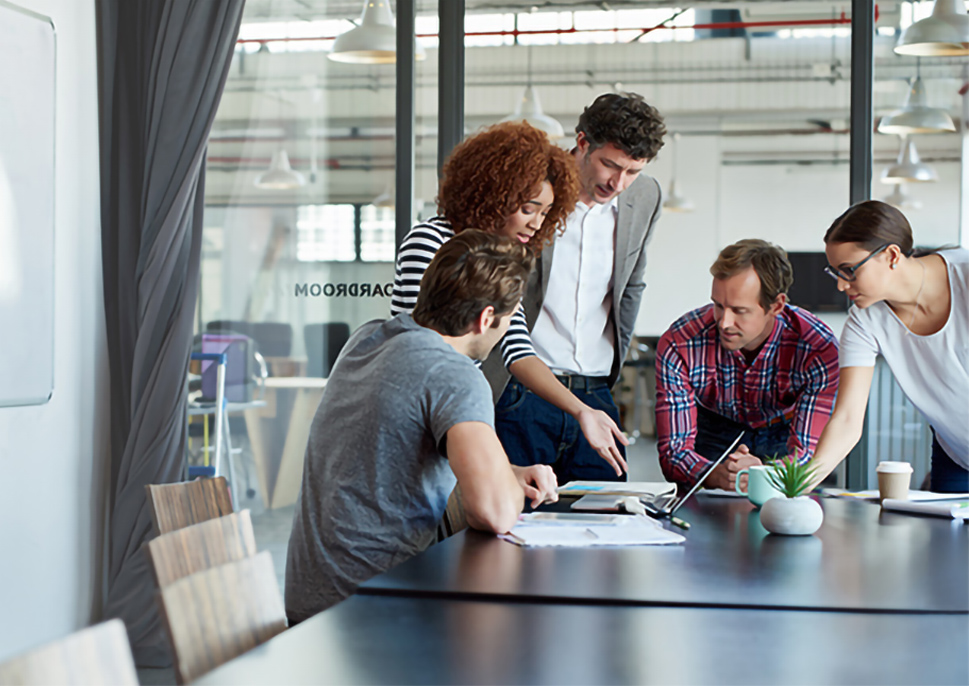 People in office meeting room gathered around a laptop