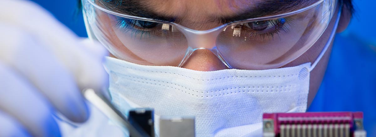 Technician in goggles and mask working on delicate equipment