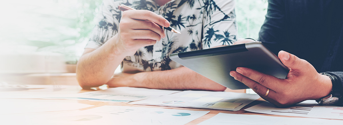 Two people looking at a tablet and printed reports