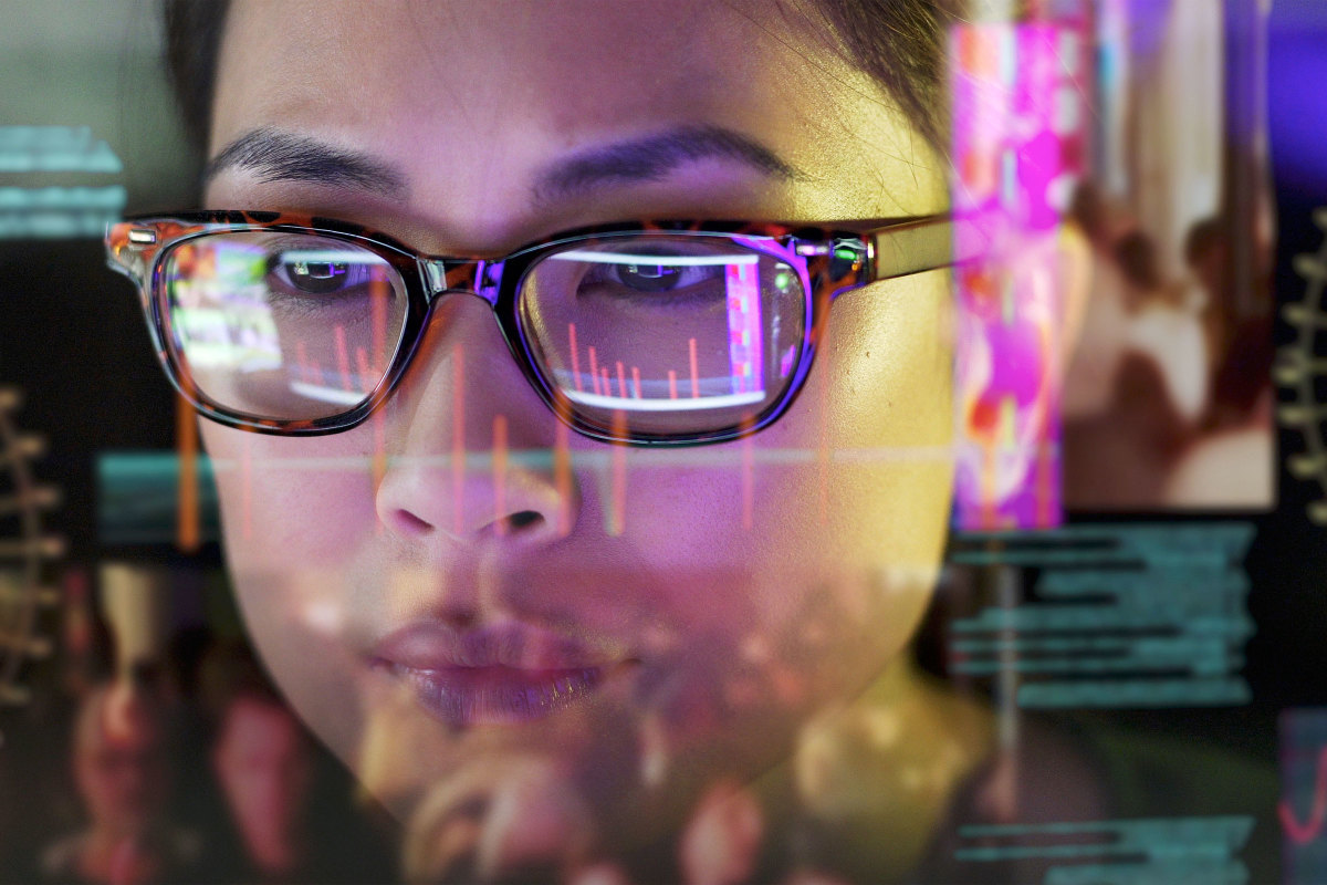 Woman with glasses studying data on a transparent screen