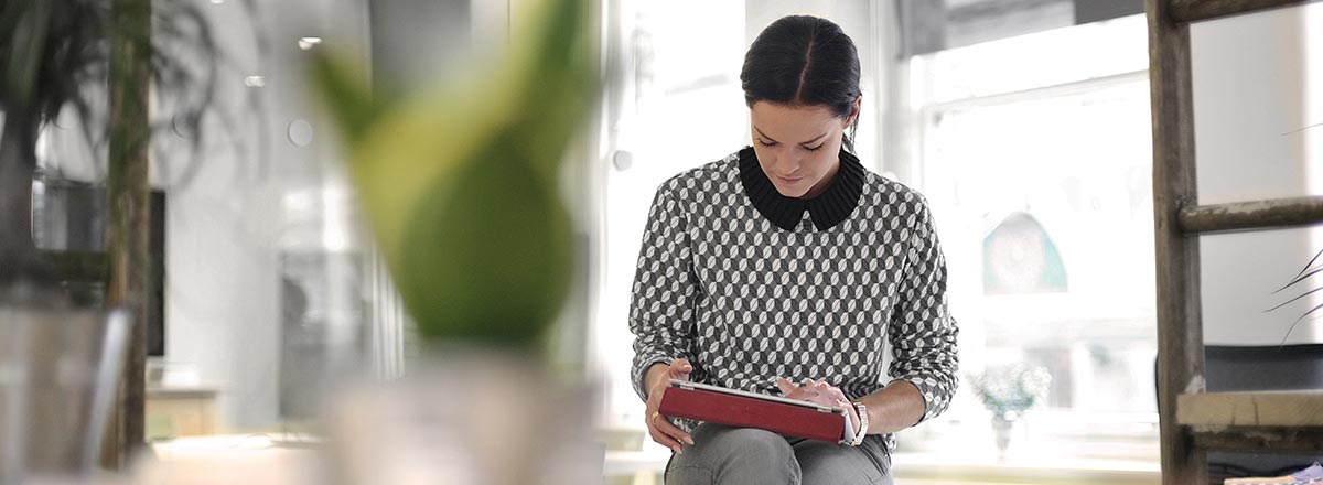 Woman in an office using a tablet, with a blurred plant near the camera