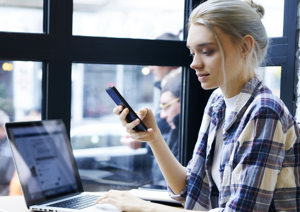 Woman in a coffee shop using a smartphone and laptop