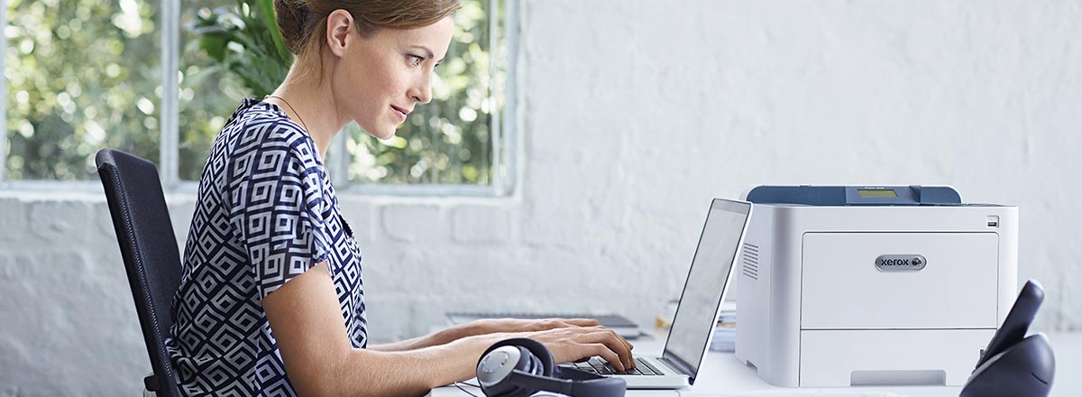 Woman in a bright office using a laptop next to a Xerox printer