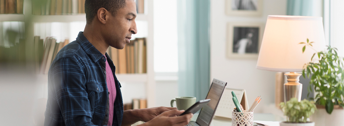 Man in home office, using smartphone and laptop