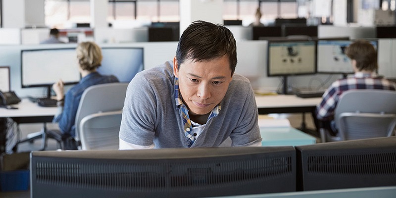 Man in an office looking at two computer monitors side by side