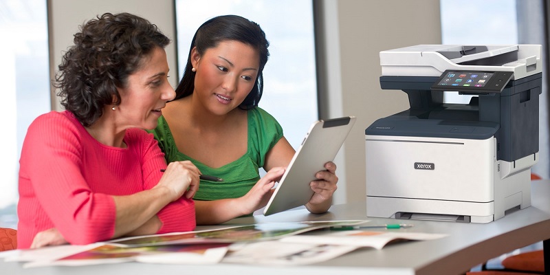 Two women reviewing forms on a tablet next to a Xerox C415 MFP