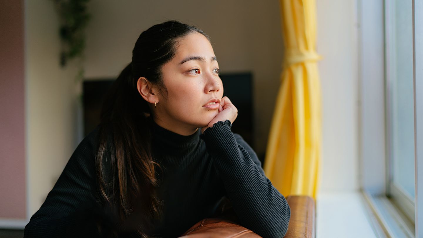 young Asian woman sitting in window deep in thought couch