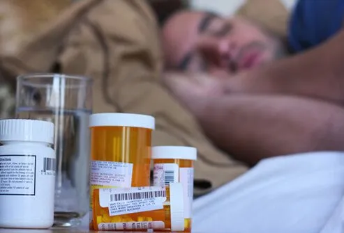 A man resting with fluids and medicine by his bed recovering from bronchitis.