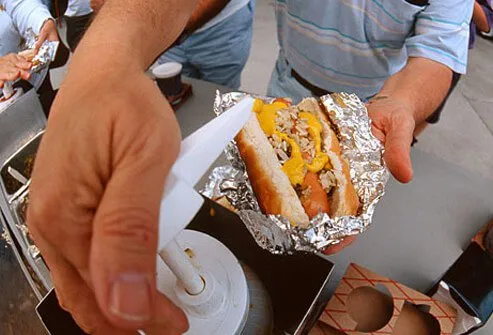 A man putting mustard onto a ballpark frank.