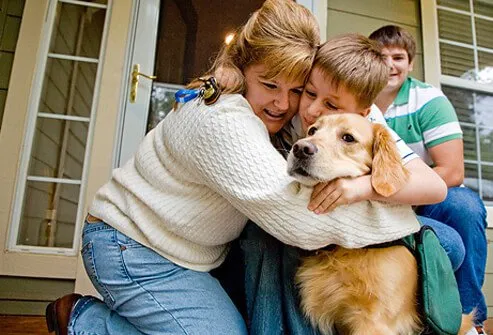 A mother hugging her son and dog.