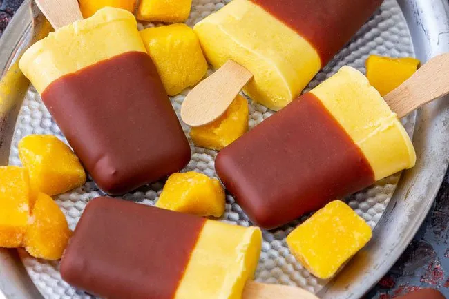 You can make frozen fruit pops by dipping mango slices on skewers into melted chocolate. 