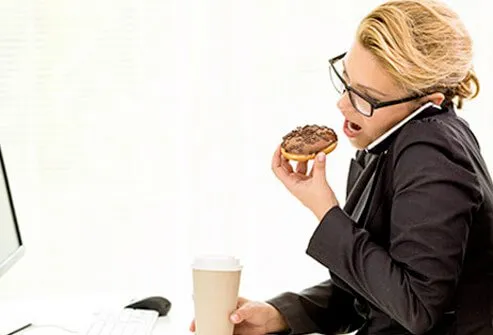 A woman eating a donut at her desk.