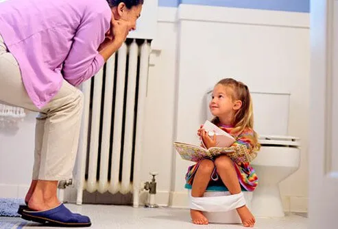 A mother watching as her daughter sits on the potty.