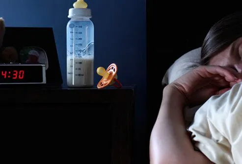 A mother sleeping with a baby bottle and pacifier on the nightstand.