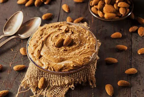 Almond butter in a bowl on a wooden table surrounded by almonds