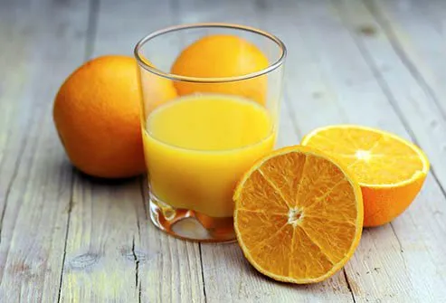 Glass of orange juice surrounded by half and whole oranges