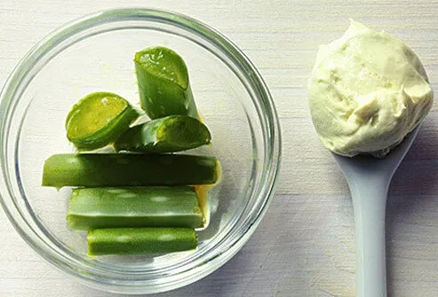 Cut aloe vera leaves in a bowl next to a scoop of lotion.