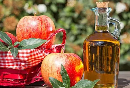 A photo of apples and vinegar on a table.