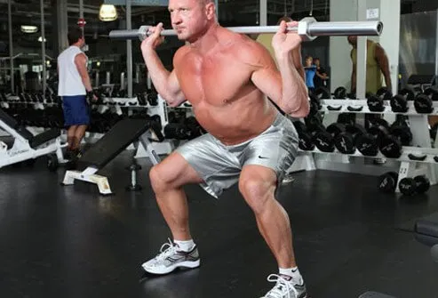 Photo of a man doing squats with a barbell.