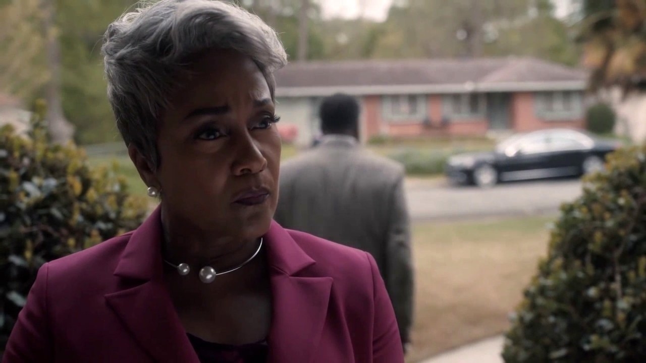 Jen Harper outside a house, looking toward the entrance while another character is walking away