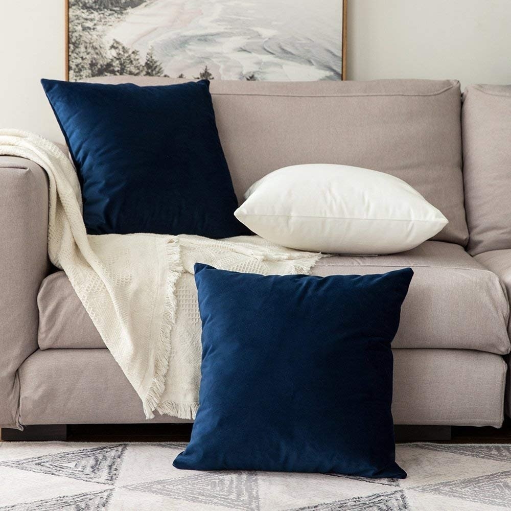 Blue and white velvet cushion covers on a sofa in front of a painting