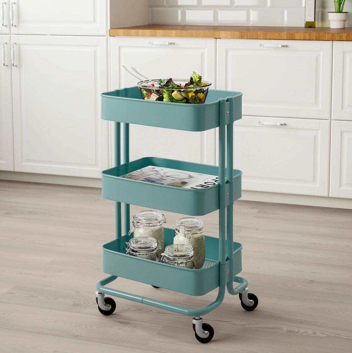 An Ikea storage cart with jars, magazines and a bowl of vegetables