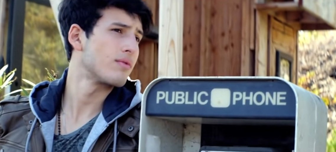 Sebastián in a leather jacket leaning on a public pay phone