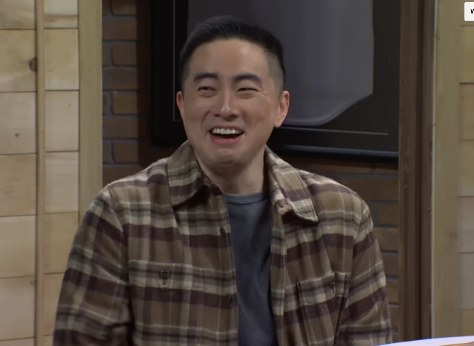 Bowen Yang in a plaid shirt smiling warmly while sitting indoors