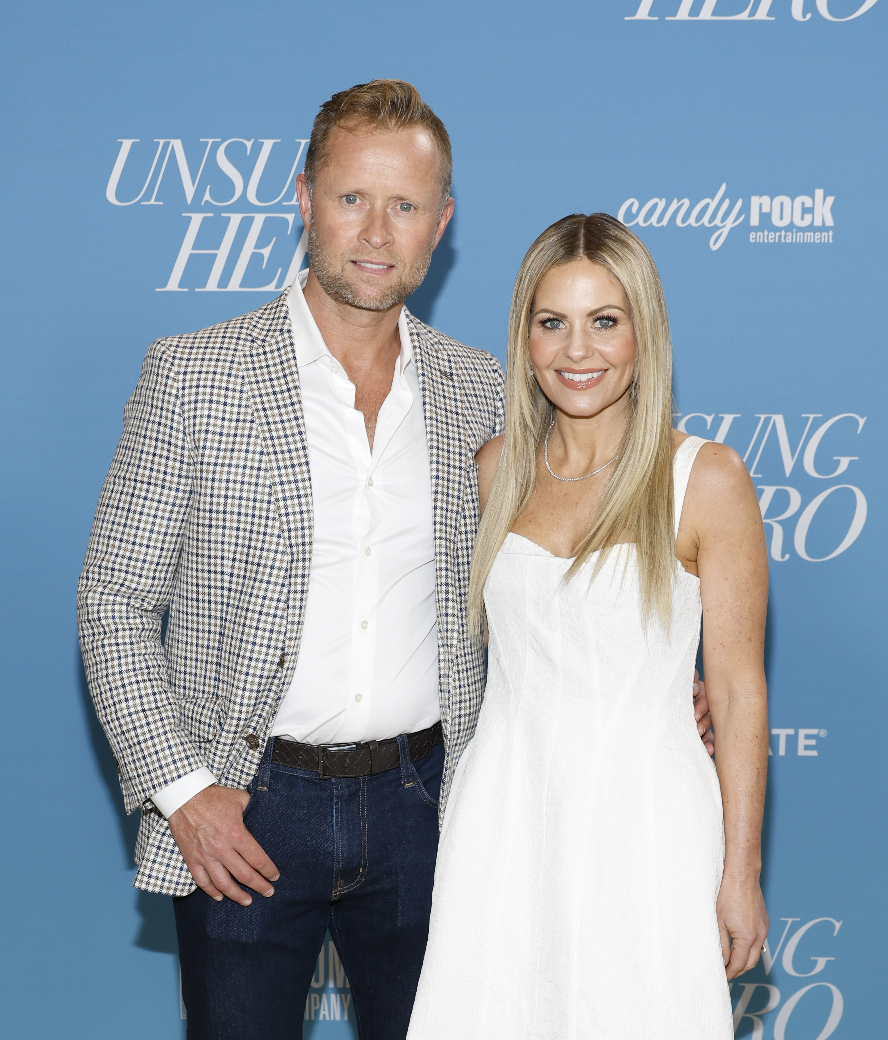 Man in a checkered jacket and white shirt with a woman in a white sleeveless dress, both smiling