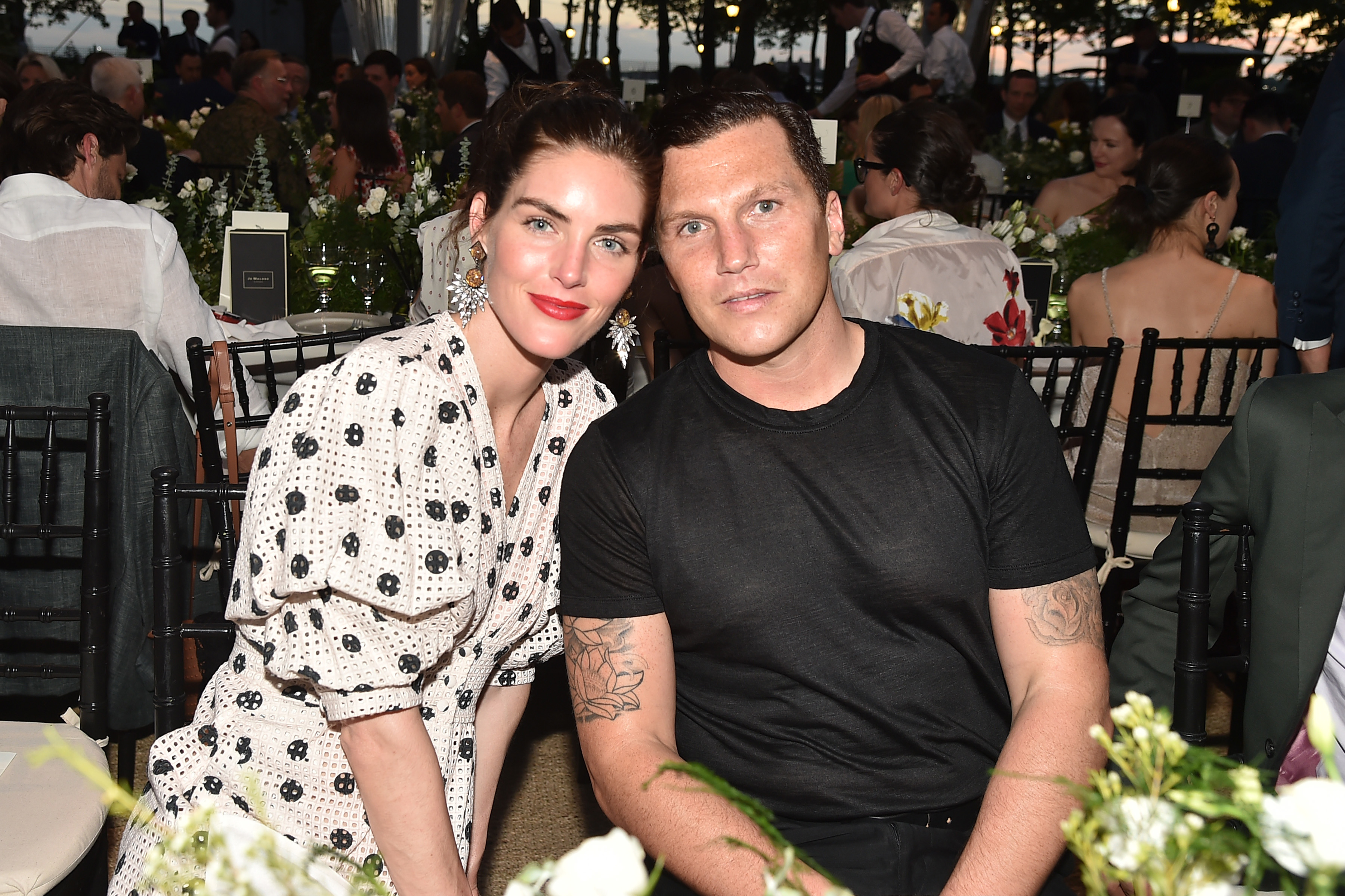 Two people seated at an event table, the woman in a polka dot dress and the man in a black shirt