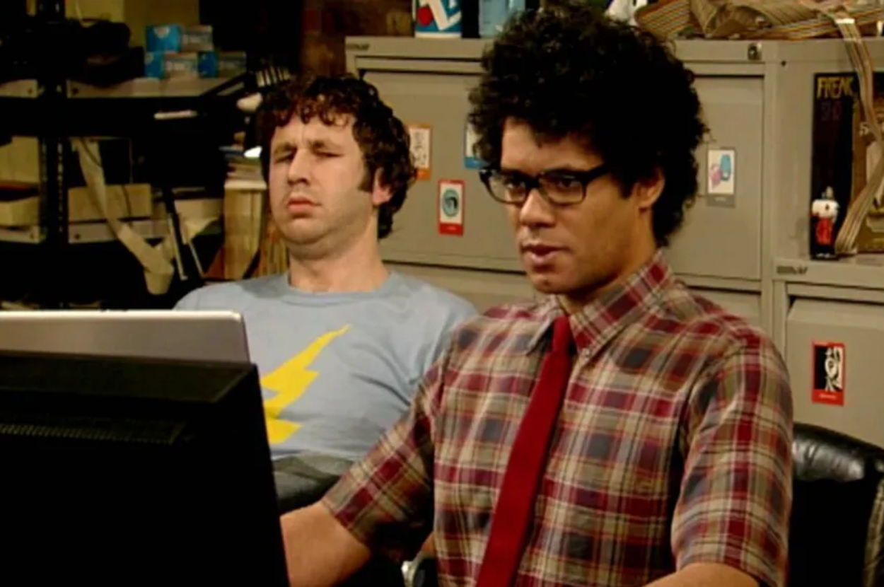 Chris O&#x27;Dowd in a blue shirt with a yellow lightning bolt and Richard Ayoade in a plaid shirt with a red tie appearing on the set of The IT Crowd