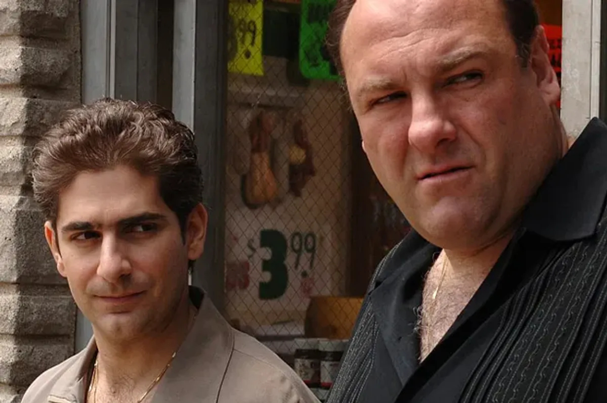 Michael Imperioli and James Gandolfini from The Sopranos, both in casual attire, stand outdoors near a storefront