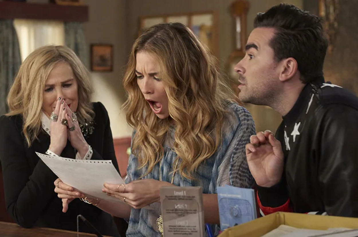 Catherine O&#x27;Hara, Annie Murphy, and Dan Levy are looking shocked at a piece of paper in a scene from a TV show