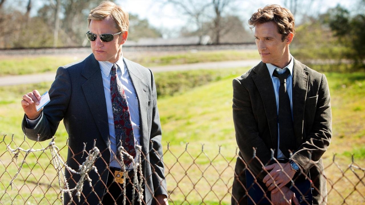 Woody Harrelson and Matthew McConaughey in suits, investigating a scene behind a fence, from the TV show &quot;True Detective&quot;