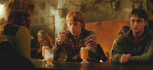 Emma Watson, Rupert Grint, and Daniel Radcliffe sitting at a pub table with drinks, engaged in conversation. They are dressed in casual, everyday clothing