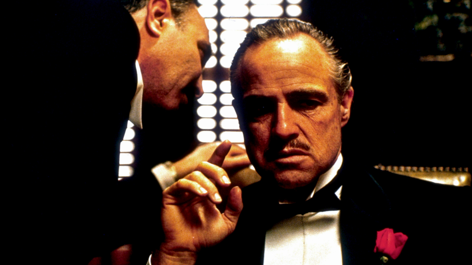 Marlon Brando as Vito Corleone in a formal suit, with another person whispering in his ear, in a scene from &quot;The Godfather.&quot;