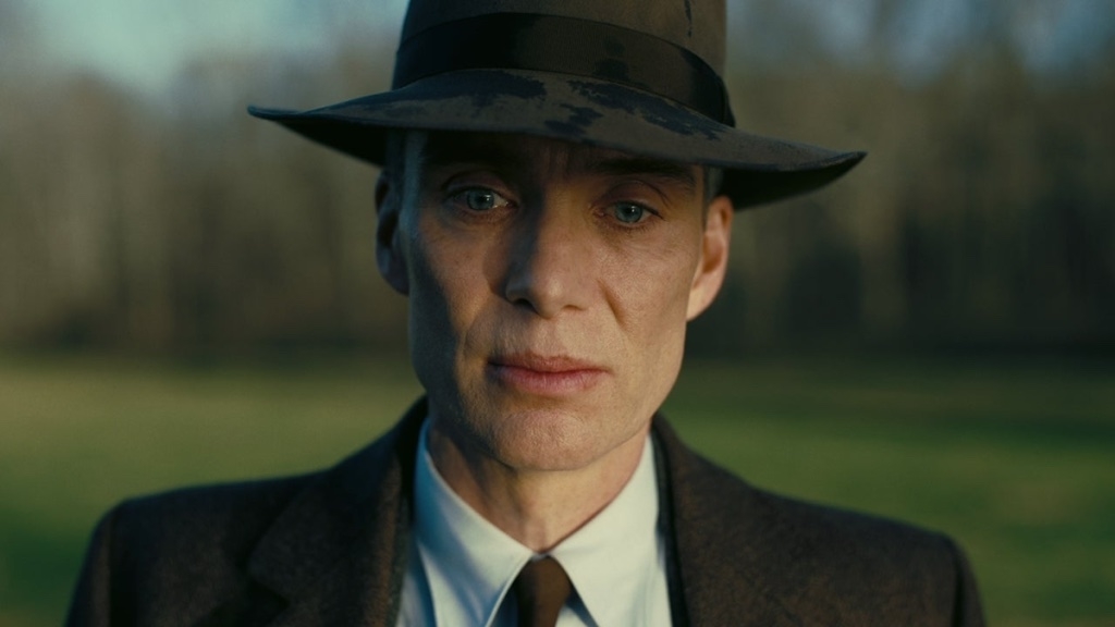 Cillian Murphy dressed in a vintage suit and hat, staring ahead with a serious expression, in a scene from a TV show or movie