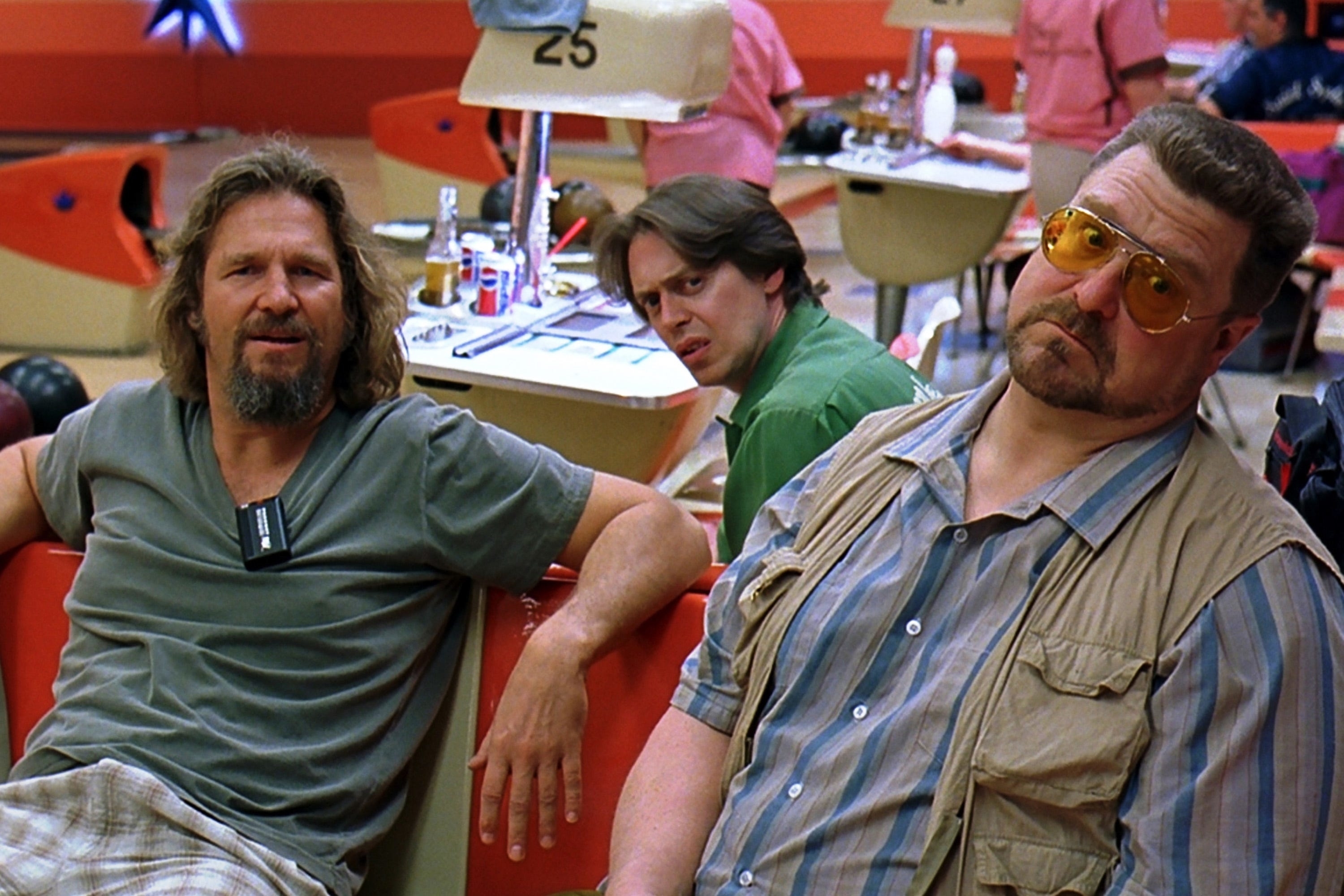 Jeff Bridges, Steve Buscemi, and John Goodman are seated in a bowling alley scene from a movie