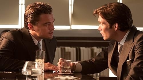 Leonardo DiCaprio and Cillian Murphy in suits, seated at a table, engaged in conversation