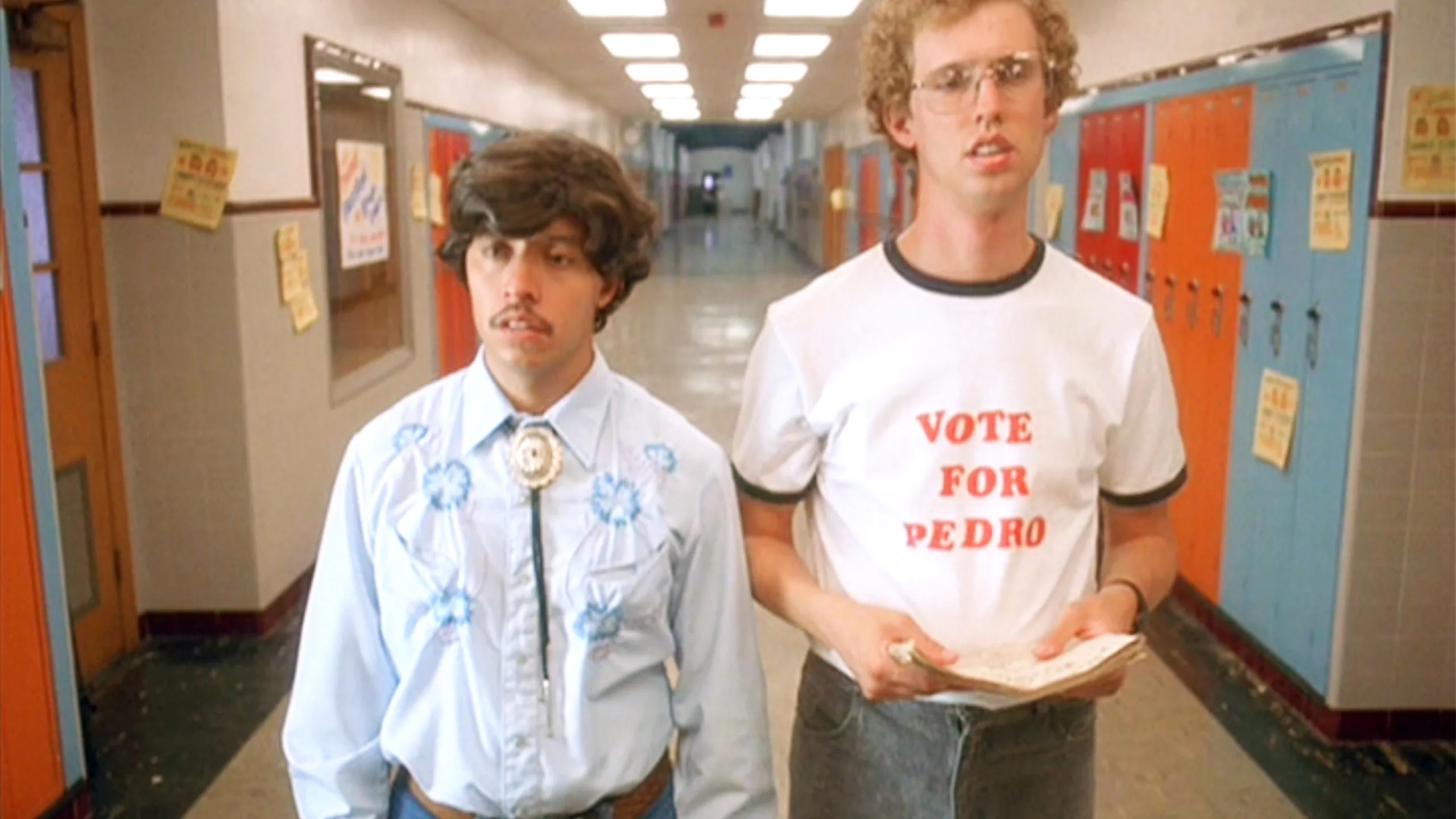 Napoleon Dynamite wears a &quot;Vote for Pedro&quot; t-shirt, and Pedro Sanchez wears a western-style shirt, standing in a school hallway with lockers in the background