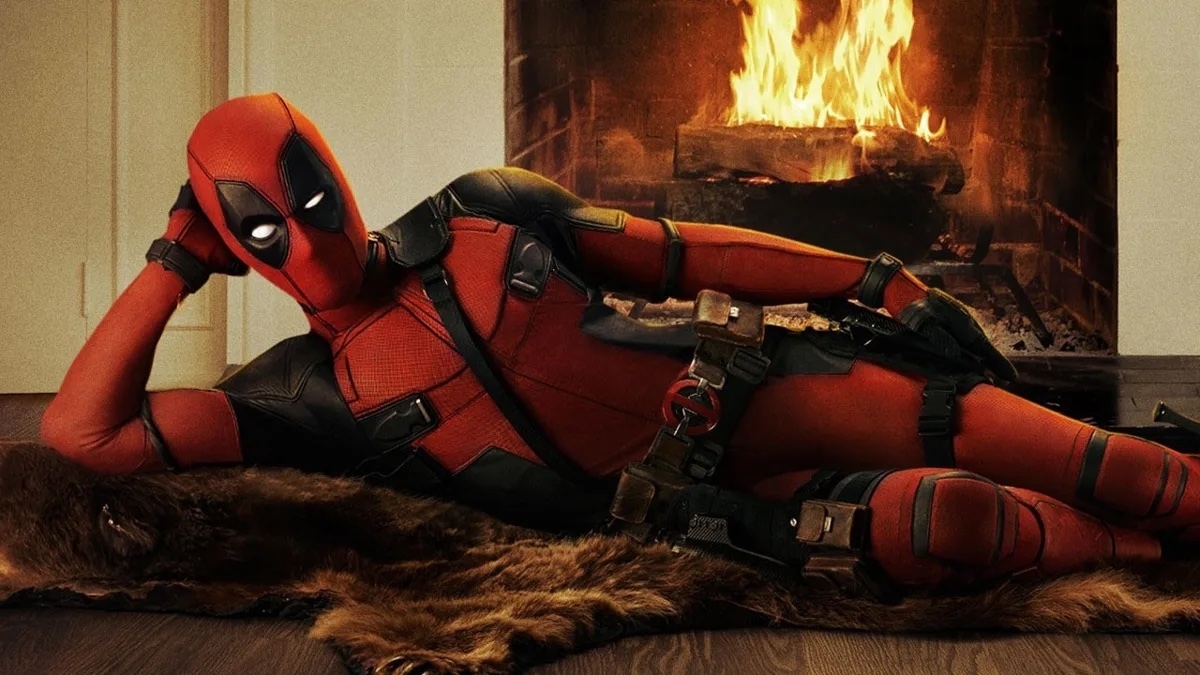 Deadpool lounges by a fireplace wearing his iconic red and black suit with utility belts and weapons, striking a humorous and relaxed pose