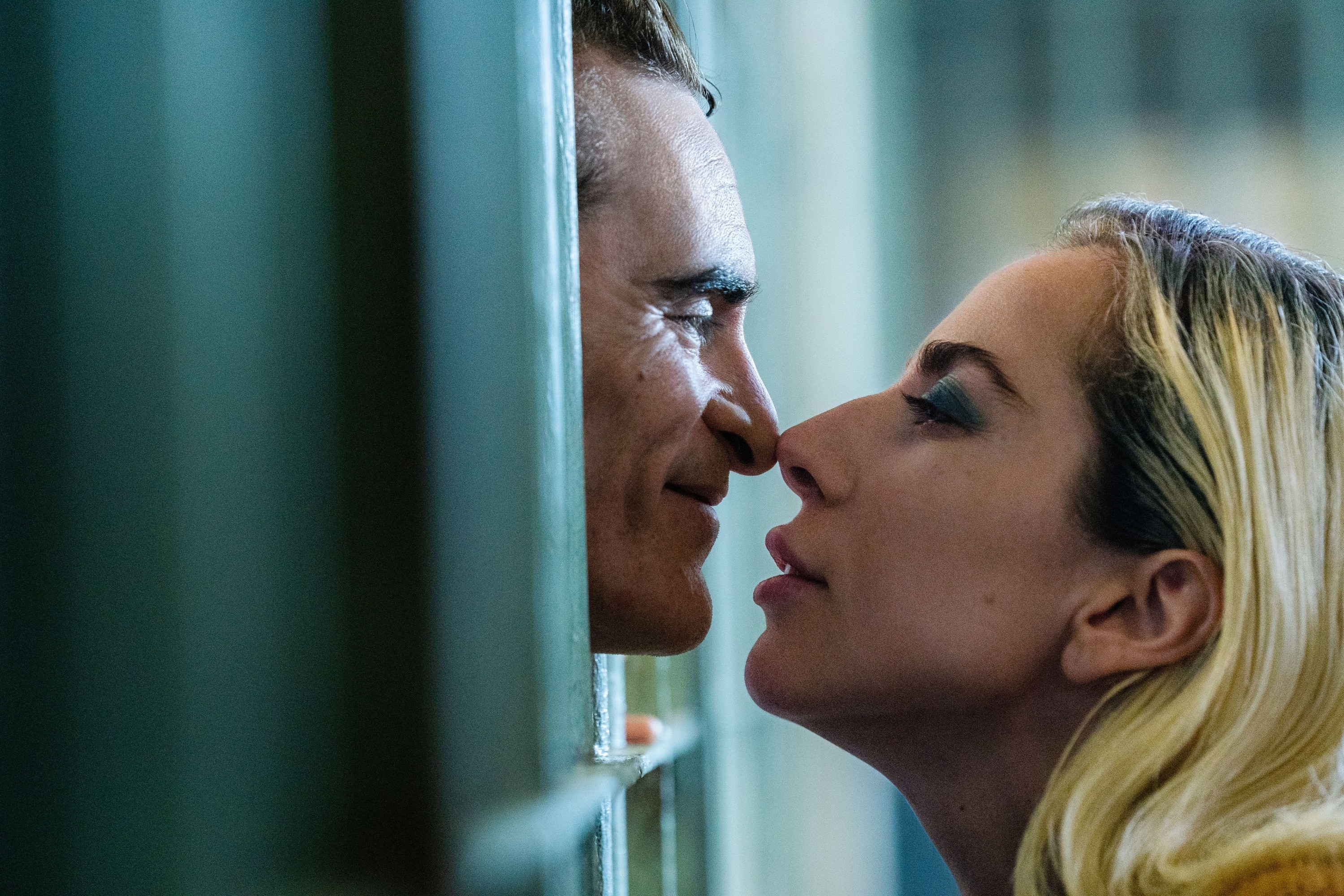 Joaquin Phoenix and Lady Gaga share an intense moment through a barred window. Both are in close proximity, creating a dramatic and emotional scene