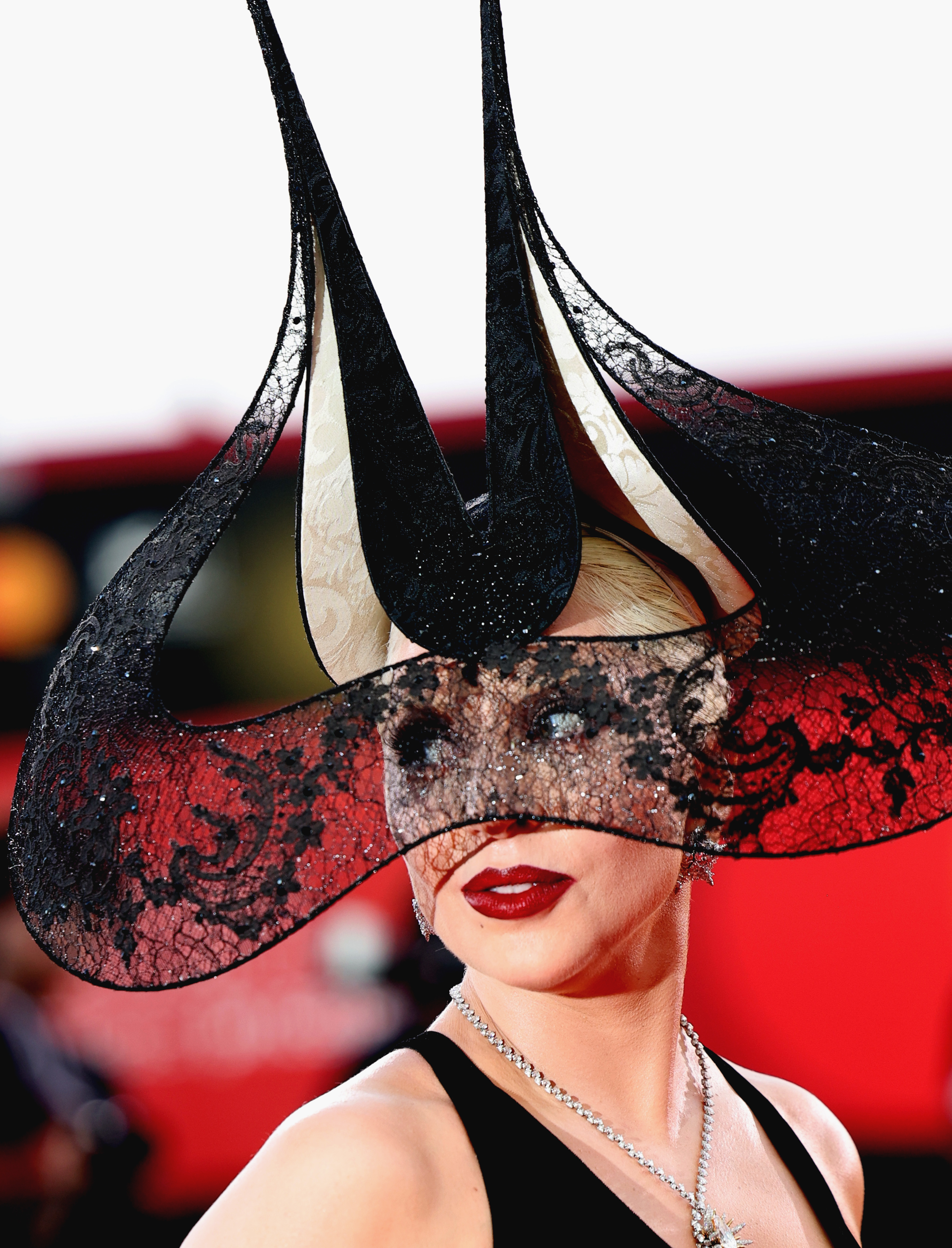 Lady Gaga on the red carpet wearing an elaborate lace headdress with high, curved spikes and a necklace